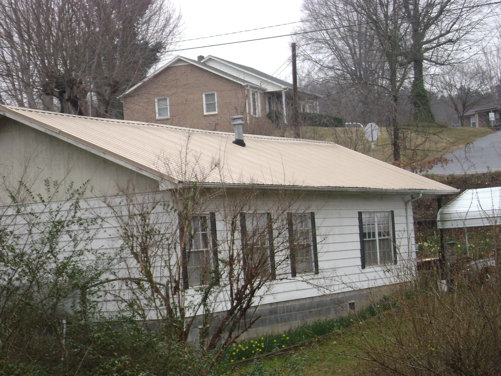 Tan metal roof on a white sided house set into a hillside — Commercial Roofing by Roofing Brothers in Mill Creek